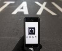 Photo illustration of logo of car-sharing service app Uber on a smartphone over a reserved lane for taxis in a street in Madrid