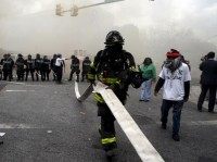 A Baltimore firefighter pulls a hose through crowds of protestors, who later cut the hose, in front of a burning building during clashes in Baltimore