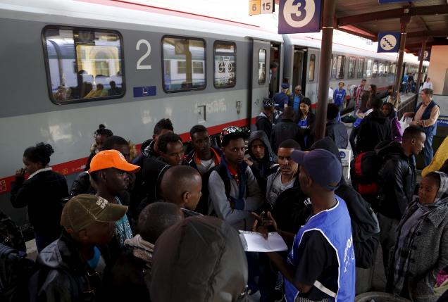 A volunteer talks to a group of migrants as police officers stand in front of the door of a train bound for Munich at the Bolzano railway station