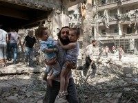 A Syrian man carries his two girls across rubble following a barrel bomb attack on Aleppo's rebel-held al-Kalasa neighbourhood