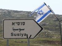 An Israeli flag flies near a sign indicating the way to the Palestinian village of Susya, south-east of Hebron, in the Israeli-occupied West Bank, on February 10, 2016.