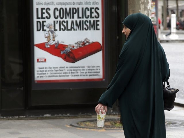 A muslim woman walks by a ad poster for French magazine Marianne reading "Radical Islam Accomplice", during a  presentation of security measures at Champs Elysees avenue in Paris, France, Thursday, May 21, 2015. (AP Photo/Francois Mori)