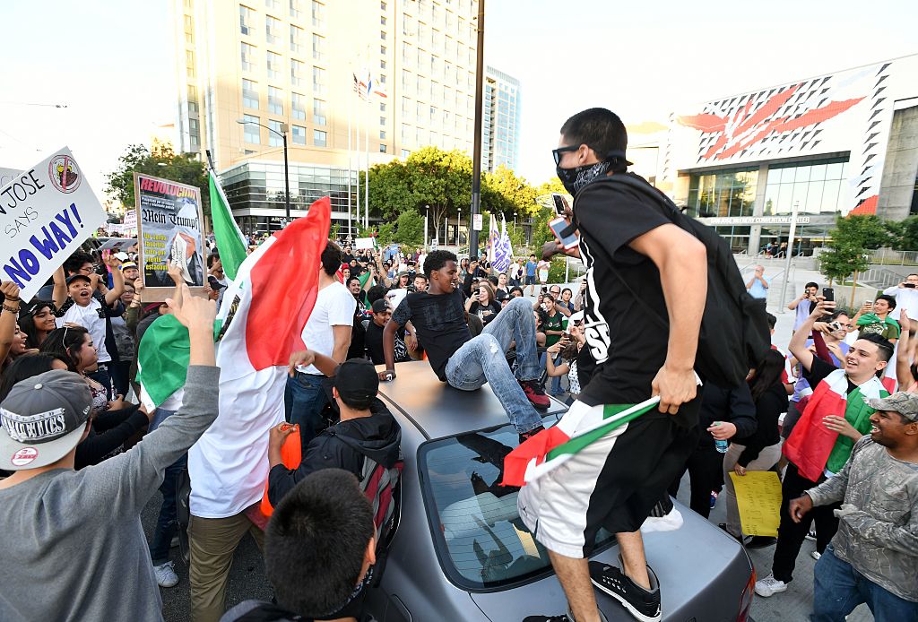 Protesters climb atop a car stopped in traffic as a crowd marches near the venue where Republican presidential candidate Donald Trump was speaking during a rally in San Jose, California on June 2, 2016. Protesters who oppose Donald Trump scuffled with his supporters on June 2 as the presumptive Republican presidential nominee held a rally in California, with fistfights erupting and one supporter hit with an egg. / AFP / JOSH EDELSON (Photo credit should read JOSH EDELSON/AFP/Getty Images)