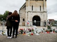 People stand in front of a make shift memorial in front of the Saint-Etienne du Rouvray church on July 27, 2016, after the priest Jacques Hamel was killed on July 26 in his church during a hostage-taking claimed by Islamic State group. France probes an attack on a church in which two men described by the Islamic State group as its 'soldiers' slit the throat of a priest.