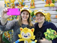 Shoppers at a megastore in Rio de Janeiro that sells official products for the 2016 Olympic and Paralympic Games wear hats in the shape of Vinicius, the official mascot of the Rio Olympics, as they pose for a photo on July 17, 2016 ahead of the opening of the Summer Games on August 5. (Photo by Kyodo News via Getty Images)