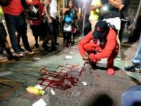A man squats near a pool of blood after a man was injured during a protest of Tuesday's fatal police shooting of Keith Lamont Scott in Charlotte, N.C. on Wednesday, Sept. 21, 2016. Protesters rushed police in riot gear at a downtown Charlotte hotel and officers have fired tear gas to disperse the crowd. At least one person was injured in the confrontation, though it wasn't immediately clear how. Firefighters rushed in to pull the man to a waiting ambulance. (AP Photo/Chuck Burton)