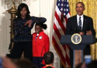 WASHINGTON, DC - SEPTEMBER 29:  U.S. first lady Michelle Obama(L) rests her elbow on the head of Olympian Simone Biles (2nd L) as President Barack Obama (R) speaks during an East Room event at the White House September 29, 2016 in Washington, DC. President Obama and the first lady welcome the 2016 U.S. Olympic and Paralympic teams to the White House to honor their participation and success in the Rio Olympic Games this year.  (Photo by Alex Wong/Getty Images)