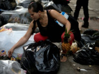 This June 2, 2016 photo shows a pregnant woman who did not want to be named, holding a pineapple in one hand as she continues to pick through garbage bags outside a supermarket in downtown Caracas, Venezuela. Unemployed people converge every dusk at the trash heap to pick through rotten fruit and vegetables tossed out by nearby shops. (AP Photo/Fernando Llano)