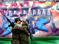 Palestinian Hamas actors dressed up as suicide bombers, one of Hamas (L) and the other of the al-Aqsa Martyrs Brigades, in a play depicting them planning the attack on the Israeli port in Ashdood in front of a painting of former Hamas spiritual leader Sheikh Ahmed Yassin, a burning Star of David, and the Israeli Knesset, during a Hamas rally April 2, 2004 at the Jabalya refugee camp in the Gaza Strip. Thousands of Hamas supporters attended the rally for a memorial service of Hamas founder and spiritual leader Sheikh Ahmed Yassin who was assassinated by Israel on March 22. (Photo by Abid Katib/Getty Images)