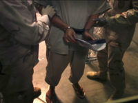 In this March 30, 2010 photo made through one way glass and reviewed by the U.S. military, a handcuffed Guantanamo detainee carries a workbook as he is escorted by guards after attending "Life Skills" class in the Camp 6 high-security detention facility on Guantanamo Bay U.S. Naval Base in Cuba. The Obama administration is pushing to close the Guantanamo detention facility by transferring, prosecuting or releasing the remaining detainees. (AP Photo/Brennan Linsley)