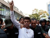 Opposition leader Leopoldo Lopez, dressed in white and holding up a flower stem, is taken into custody by Bolivarian National Guards, in Caracas, Venezuela, Tuesday, Feb 18, 2014. Lopez re-emerged from days of hiding to address an anti-government demonstration and then he turned himself in to authorities Tuesday. Speaking to some 5,000 supporters with a megaphone, Lopez said that he doesn't fear going to jail to defend his beliefs and constitutional right to peacefully protest against President Nicolas Maduro. (AP Photo/Alejandro Cegarra)