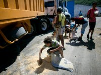 In this Nov. 14, 2016 photo, a youth uses his pillow as a bag to collect rice from the pavement that shook loose from a food cargo truck waiting to enter the port in Puerto Cabello, Venezuela, the port that handles the majority of Venezuela's food imports. As millions of Venezuelans go hungry this year, food trafficking has become one of the most lucrative businesses in the country. (AP Photo/Ariana Cubillos)