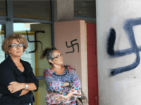 Teachers stand next next to a swastika painted onto a wall of the high school in Agde, in southern France, on September 4, 2008. Some forty swastikas as well as other racist affronts were painted on the night of September 3-4 by one or many unknown persons on the walls of the school. French Education Minister Xavier Darcos 'condemned with upmost firmness these acts of vandalism of a racist character, antisemitism and xenophobia'. AFP PHOTO/BORIS HORVAT (Photo credit should read BORIS HORVAT/AFP/Getty Images)
