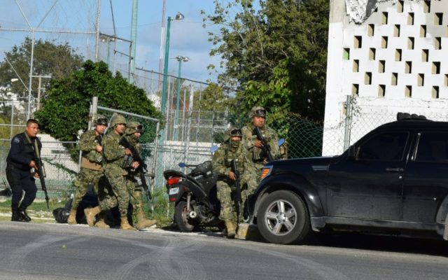 Police and soldiers take cover during an attack on the Quintana Roo state prosecutor's office in Cancun, Mexico, which left the gunman and two staff dead