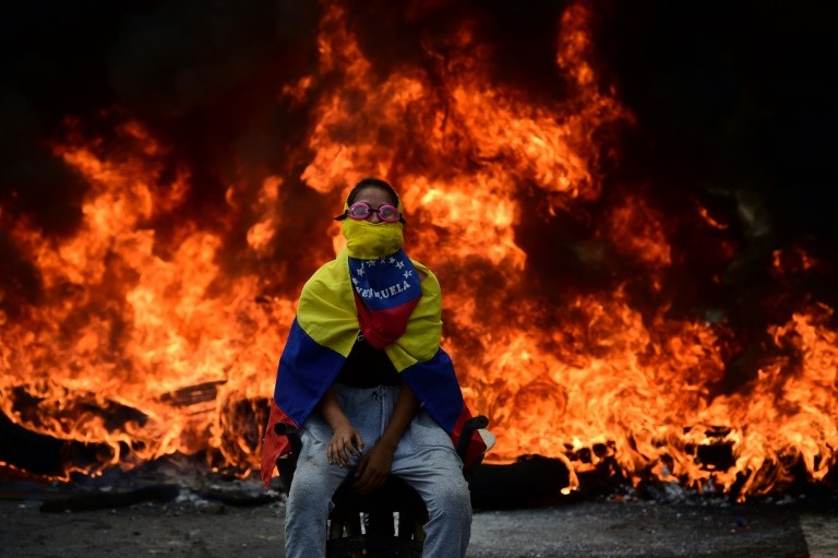 A Venezuelan opposition activist is backdropped by a burning barricade during a demonstration against President Nicolas Maduro in Caracas, on April 24, 2017