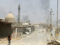TOPSHOT - An Iraqi boy rides a bicycle in west Mosul's al-Saha neighbourhood on May 29, 2017 as smokes billows during ongoing battles by Iraqi forces to retake the city from Islamic State (IS) group fighters. Iraqi forces pressed forward with a broad offensive targeting Islamic State group-held areas in west Mosul and called for civilians to leave areas where fighting is taking place. / AFP PHOTO / KARIM SAHIB (Photo credit should read KARIM SAHIB/AFP/Getty Images)