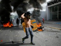 An anti-government demonstrator walks past two National Guard soldiers' motorcycles that were set on fire by protesters when the soldiers ran from their bikes after falling during clashes with protesters in Caracas, Venezuela, Wednesday, May 31, 2017. Protesters have flooded the streets of Venezuela for months, demanding new elections and faulting President Nicolas Maduro's leadership for the country's triple-digit inflation, surging crime rates, and dire shortages of food and medicine. (AP Photo/Ariana Cubillos)