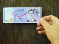 In this photo released by the Syrian official news agency SANA, a man displays a new bank note of 2,000 Syrian Lira, ($3.9), during a press conference for the Central Bank Governor Duraid Durgham in Damascus, Syria, Sunday, July 2, 2017. The notes are the first time the face of President Bashar Assad appears on the Syrian currency since he took office 17 years ago. (SANA via AP)