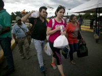 Venezuelans carrying their purchases return to their country through the Simon Bolivar bridge in Cucuta, Colombia, Sunday, July 17, 2016. Tens of thousands of Venezuelans crossed the border into Colombia on Sunday to hunt for food and medicine that are in short supply at home. It's the second weekend in a row that Venezuela's government has opened the long-closed border connecting Venezuela to Colombia. (AP Photo/Ariana Cubillos)