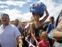 FILE - In this July 17, 2016 file photo, a woman carrying a bundle on her head waits in line to cross the border into Colombia through the Simon Bolivar International Bridge in San Antonio del Tachira, Venezuela. An estimated 25,000 Venezuelans trek across the international bridge into Colombia each day. Many come for a few hours to work or trade goods on the black market. But increasingly, they are coming to eat in one of a half-dozen facilities offering the increasingly hungry Venezuelans a free plate of food. (AP Photo/Ariana Cubillos, File)