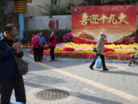 In this Oct. 16, 2017 photo, residents pass by a board with the words "Welcome the 19th Congress" on the streets of Beijing, China. Extraordinary security measures are being imposed ahead of the party congress, in addition to the typical security forces, thousands of deputized citizens patrol the streets, and knife, fireworks and chemical sales have been suspended. (AP Photo/Ng Han Guan)