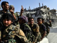 Kurdish fighters of the Syrian Democratic Forces (SDF) ride in the back of a truck passing damaged buildings in Raqa on October 20, 2017, after a Kurdish-led force expelled the Islamic State group from the northern Syrian city. For three years, Raqa saw some of IS's worst abuses and grew into one of its main governance hubs, a centre for both its potent propaganda machine and its unprecedented experiment in jihadist statehood. / AFP PHOTO / BULENT KILIC (Photo credit should read BULENT KILIC/AFP/Getty Images)