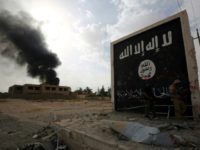 Iraqi fighters stand next to a wall bearing the Islamic State group flag in western Anbar province on November 3, 2017