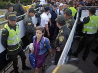 In this July 17, 2016 file photo, police stand guard as a Venezuelan woman crosses into Colombia through the Simon Bolivar bridge linking San Antonio del Tachira, Venezuela, with Cucuta, Colombia. President Juan Manuel Santos announced Thursday, Feb. 8, 2018, that more than 2,000 new officers will be dispatched to police the hundreds of unpaved, dirt road crossings migrants are using to enter Colombia illegally. Colombia will also stop issuing border cards that currently allow 1.5 million Venezuelans to temporarily enter the nation to purchase food and medicine. (AP Photo/Ariana Cubillos, File)