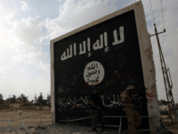 Iraqi fighters of the Hashed al-Shaabi (Popular Mobilisation units) stand next to a wall bearing the Islamic State (IS) group flag as they enter the city of al-Qaim, in Iraq's western Anbar province near the Syrian border as they fight against remnant pockets of Islamic State group jihadists on November 3, 2017. / AFP PHOTO / AHMAD AL-RUBAYE (Photo credit should read AHMAD AL-RUBAYE/AFP/Getty Images)