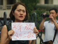 FILE - In this Aug. 1, 2016 file photo, a man films Li Wenzu, left, wife of imprisoned lawyer Wang Quanzhang, holds a paper that reads 