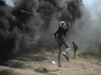 A Palestinian protester hurls stones at Israeli troops during a protest at the Gaza Strip's border with Israel, Friday, April 6, 2018. (AP Photo/ Khalil Hamra)