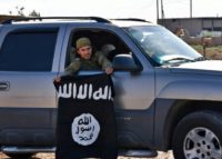 A Syrian pro-government militia member holds a captured Islamic State group flag in June 2017 outside the city of Raqa, which later fell to the Syrian Democratic Forces in October 2017