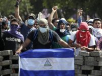 Masked protesters, one with a Nicaraguan flag, yell from the road block they erected as they face off with security forces near the University Politecnica de Nicaragua (UPOLI) in Managua, Nicaragua, Saturday, April 21, 2018. Nicaragua's government said on Saturday it is willing to negotiate over controversial social security reforms that have prompted protests and deadly clashes this week. (AP Photo/Alfredo Zuniga)