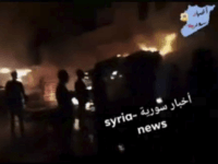 This frame grab from video provided on Wednesday, May, 9, 2018 by Syria News, shows people standing in front of flames rising after an attack on an area known to have numerous Syrian army military bases, in Kisweh, south of Damascus, Syria on Tuesday. The Britain-based Syrian Observatory for Human Rights said the missiles targeted depots and rocket launchers that likely belonged to Iran's elite Revolutionary Guard in Kisweh, killing nine people. (Syria News, via AP)