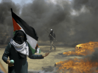A woman holds a Palestinian flag as a protester burns tires near the Israeli border fence, east of Khan Younis, in the Gaza Strip, Monday, May 14, 2018. Thousands of Palestinians are protesting near Gaza's border with Israel, as Israel prepared for the festive inauguration of a new U.S. Embassy in contested Jerusalem. (AP Photo/Adel Hana)