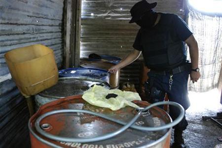 Policeman inspects barrels containing stolen diesel fuel, stored in a tyre repair shop, du