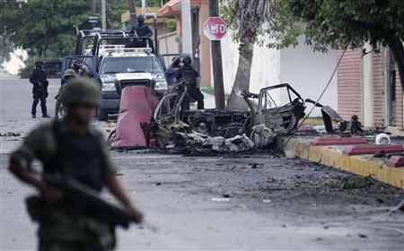 Mexican policemen and a soldier stand guard next to remains of a parked vehicle outside a