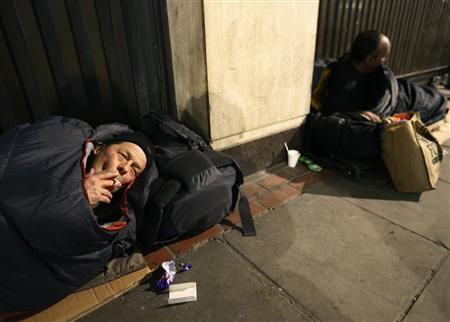 Two homeless men lie against a building near Victoria rail station in central London