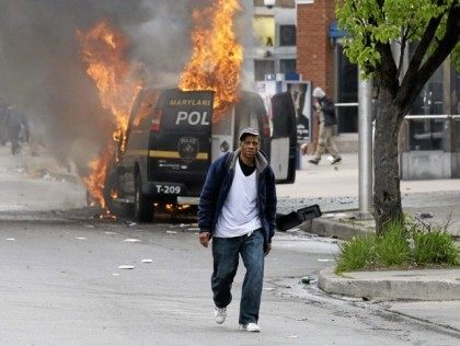 A man walks past a burning police vehicle, Monday, April 27, 2015, during unrest following the funeral of Freddie Gray in Baltimore. Gray died from spinal injuries about a week after he was arrested and transported in a Baltimore Police Department van. (AP Photo/Patrick Semansky)