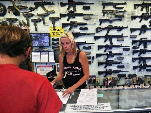In this July 20, 2014 photo, with guns displayed for sale behind her, a gun store employee helps a customer at Dragonman's, east of Colorado Springs, Colo. When Colorado lawmakers expanded background checks on firearms last year, they were expecting a huge increase. But the actual number the first 12 …