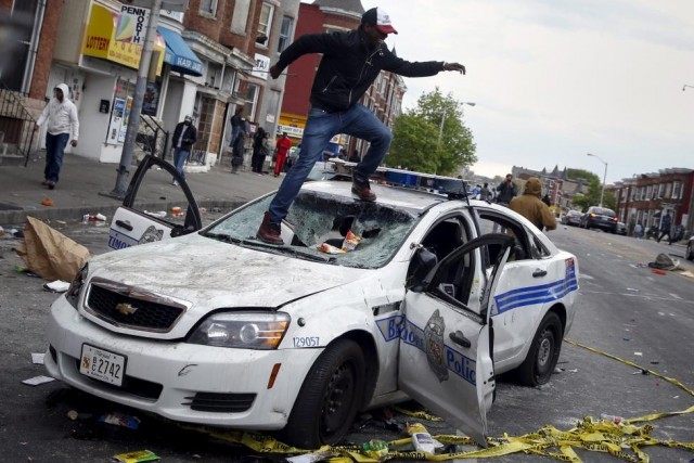 Demonstrators jump on a damaged Baltimore police department vehicle during clashes in Balt