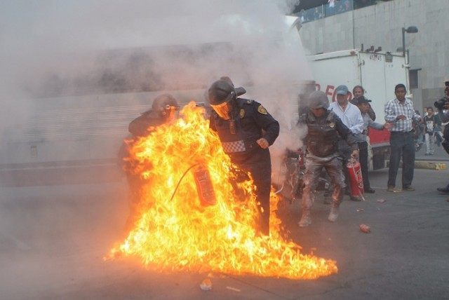 A police officer tries to fight the flames surrounding him after protesters began throwing