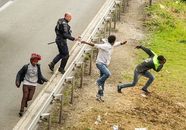 A police officer sprays tear gas to migrants trying to access the Channel Tunnel on the A1