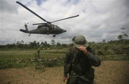 Colombian police officer protects himself from wind as helicopter takes off from coca plan