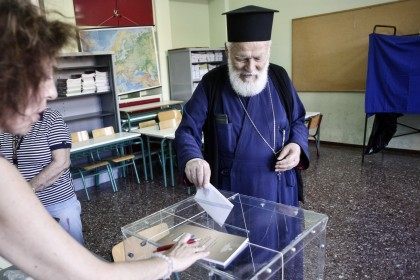 ATHENS, GREECE - JULY 5: An Orthodox priest puts a referendum vote in the ballot box at a school on July 5, 2015 in Athens, Greece. The people of Greece are going to the polls to decide if the country should accept the terms and conditions of a bailout with …