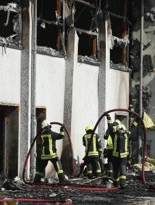 NAUEN, GERMANY - AUGUST 25:  Firemen collect their hoses after extinguishing a fire that struck a sports hall that was intended to house refugees and migrants applying for aslyum in Germany on August 25, 2015 in Nauen, Germany. 