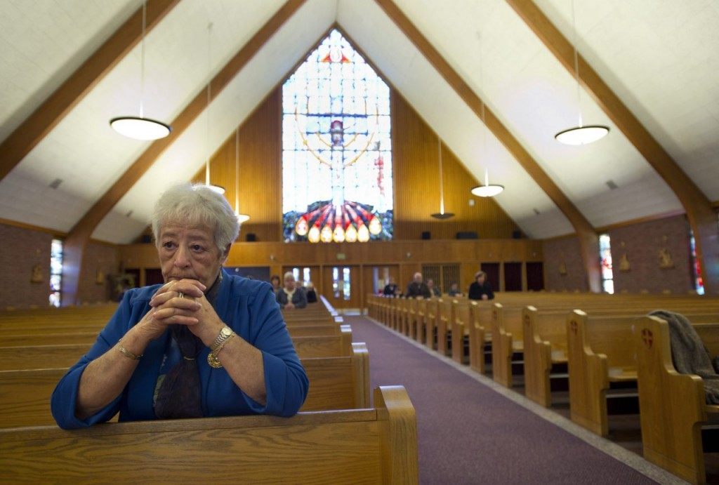 In this Sunday, Nov. 6, 2011 photo, Mary Fernandes prays during a worship service at St. Frances Cabrini Catholic Church in Scituate, Mass. Parishioners have just begun their eighth year maintaining a round-the-clock vigil to keep the church open. Until this fall, the archdiocese had paid for the heating at St. Francis X. Cabrini. Then a utility worker cut the power off, saying the bill hadn’t been paid in months. The archdiocese called it an error, but vigil leader Jon Rogers says they’re trying to stop the remaining holdouts. (AP Photo/Gretchen Ertl)
