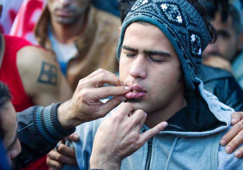 A man uses needle and thread to sew shut the mouth of a compatriot from Iran as a sign of protest as migrants and refugees wait to cross the Greek-Macedonian border near Gevgelija on November 26, 2015. Since last week, Macedonia has restricted passage to northern Europe to only Syrians, Iraqis and Afghans who are considered war refugees. All other nationalities are deemed economic migrants and told to turn back. Over 1,500 people are stuck on the border, mostly Indian, Moroccan, Bangladeshi and Pakistani. AFP PHOTO / ROBERT ATANASOVSKI / AFP / ROBERT ATANASOVSKI (Photo credit should read ROBERT ATANASOVSKI/AFP/Getty Images)