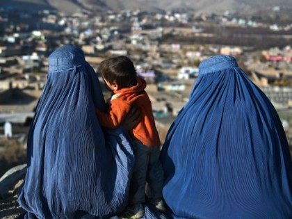 Afghan burqa clad women sit in a cemetery overlooking the outskirts of Kabul on December 1