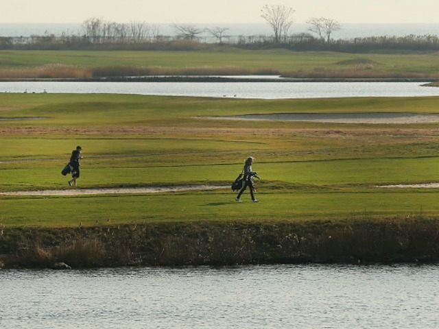 Golfers walk along the water during an afternoon of warm and sunny weather on December 13,